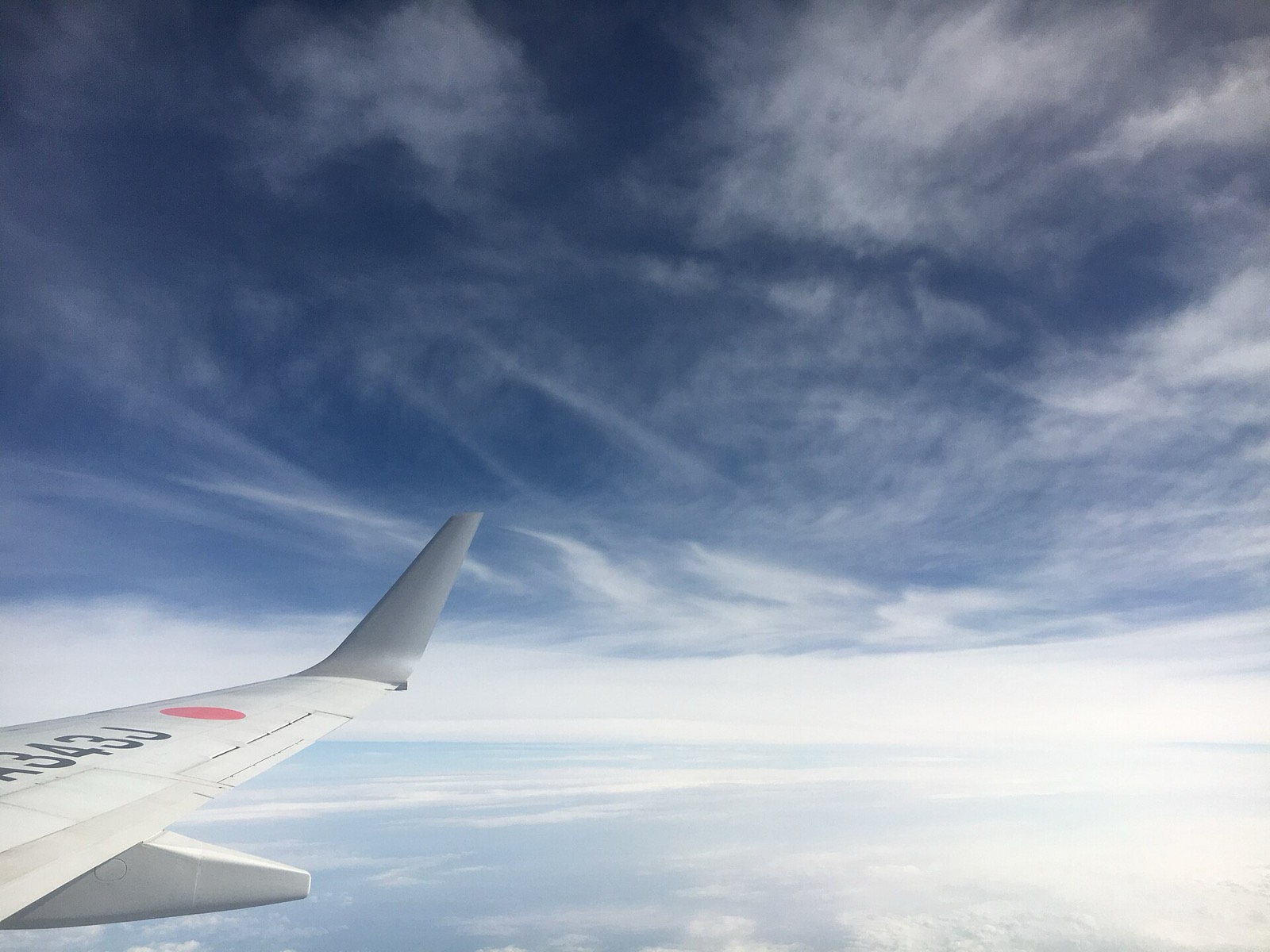 Aile d'avion au-dessus d'une couche de nuages éparse, cirrus en altitude
