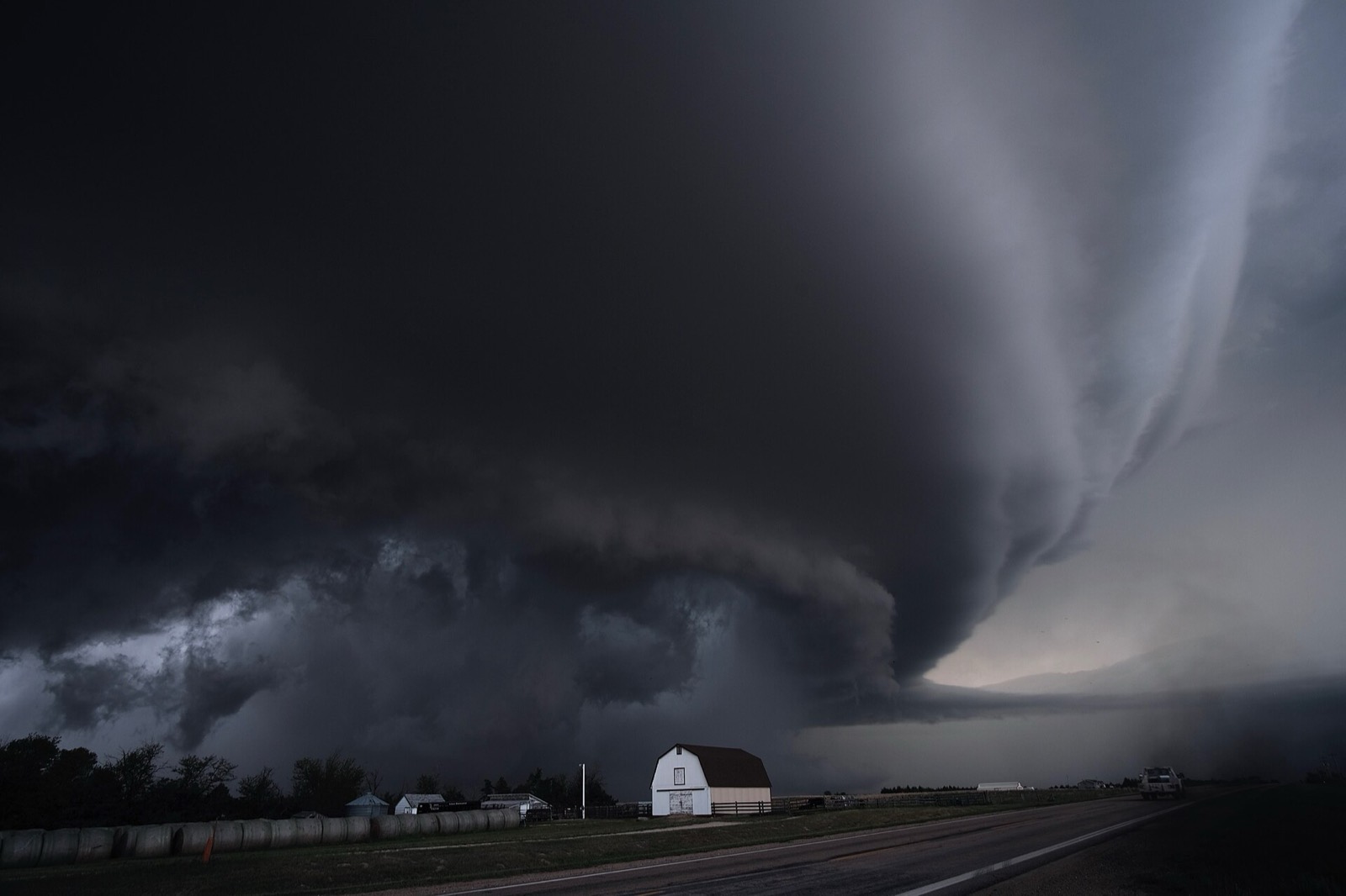Orage supercellulaire sombre au-dessus d'une plaine, avec une ferme au premier plan